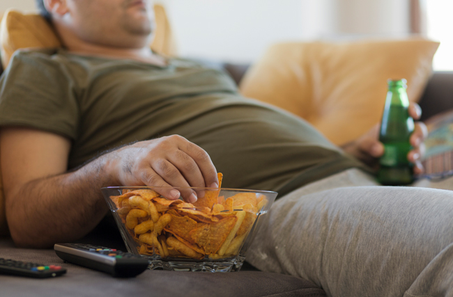 Mann liegt auf der Couch und isst Chips