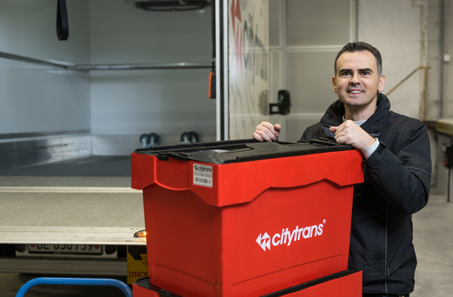 Mitarbeiter von citytrans mit einer roten Transportbox mit Logo des Speziallogistikunternehmens