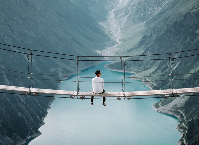Un homme assis sur un pont suspendu au-dessus d'un lac