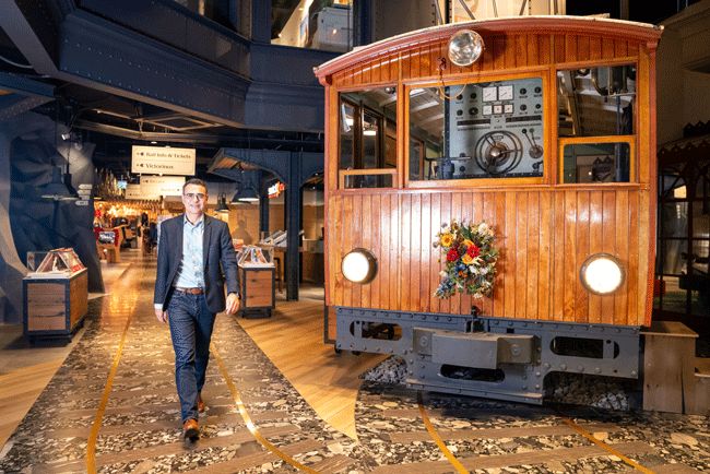 Jungfraubahnen Andreas Piattini HR-Spezialist geht neben einem ausgestellten Oldtimer aus Holz