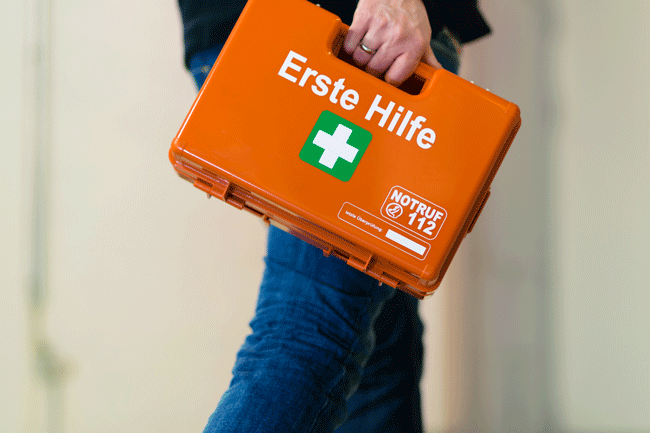 Ein Mann trägt einen Erste-Hilfe-Koffer, Symbolbild für BGM Werkzeuge der Gesundheitsförderung Schweiz