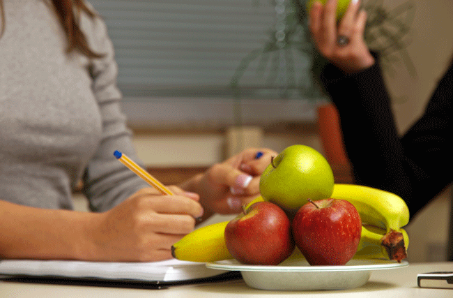 Eine Mitarbeiterin bedient sich an einer Frucht in einer Schale im Büro