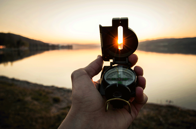 Kompass wird auf den Sonnenuntergang ausgerichtet, symbolisch für strategische Navigation