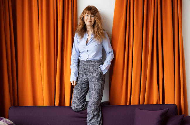 Zukunftsforscherin und Autorin von Kindness Economy Oona Strathern steht auf einer Couch vor einem orangen Vorhang
