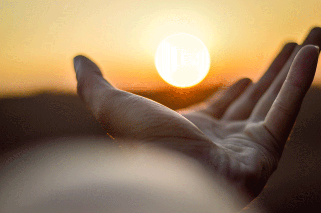 Die Sonne geht unter. Jemand hält seine Hand unter der untergehenden Sonne. Damit entsteht die Illusion, dass eine Kraftquelle von seiner Hand ausgeht.