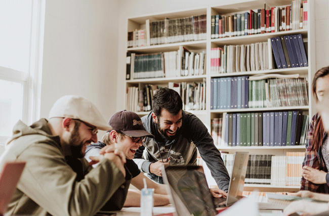 Eine Gruppe junge Mitarbeiter lachen zusammen vor ihren Computern im Büro