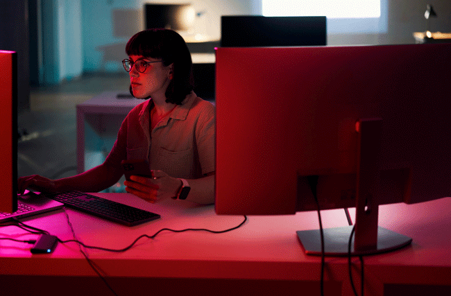 Mitarbeiterin arbeitet sich durch Personalentwicklungsprogramm am PC. Die rote Beleuchtung ist symbolisch für die ethische Gefahren
