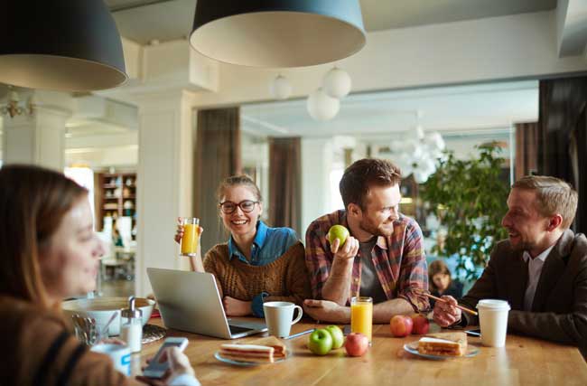 Ein Team sitzt an einem Tisch, die Mitarbeitende lachen miteinander und geniessen gesunde Früchte