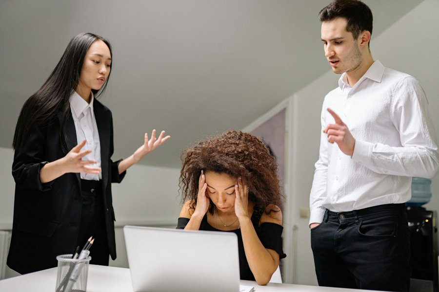 Ce qu'il faut savoir sur le harcèlement au travail: une femme et un homme invectivent une employée assise à son bureau