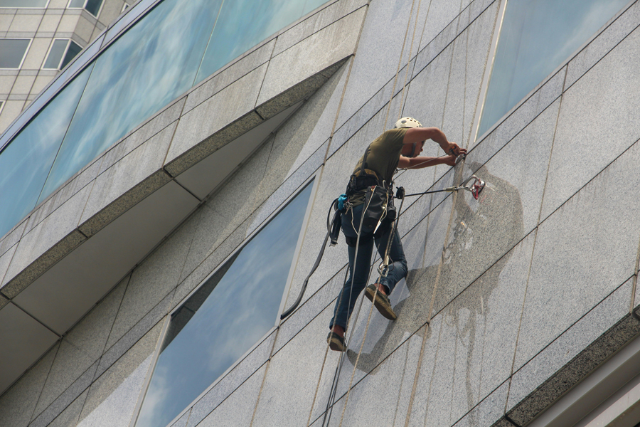 Un homme attaché à un harnais répare la facade d'un immeuble