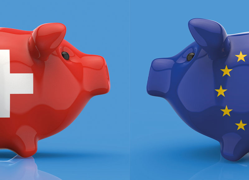 Ein Schweizer Sparschwein und ein EU-Sparschwein schauen sich gegenseitig an.