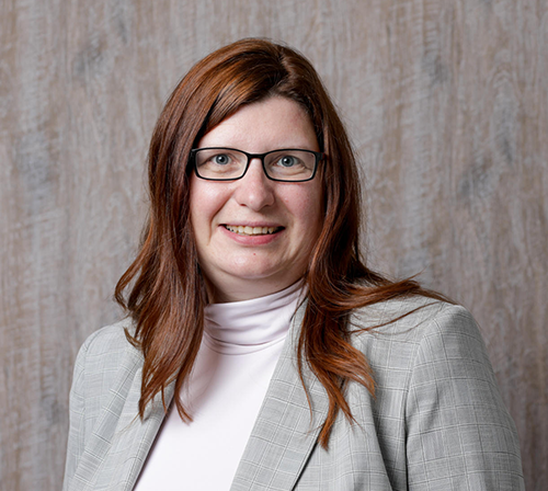 Das Bild zeigt Susanne Krüger-Lampe, eine Frau mit rotbraunen Haaren, etwas mehr als schulterlang, Brille, weissem Rollkragenpullover und grauem Blazer.