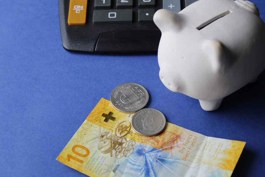 Billets de banque suisses, pièces de monnaie, tirelire et calculatrice sur fond bleu