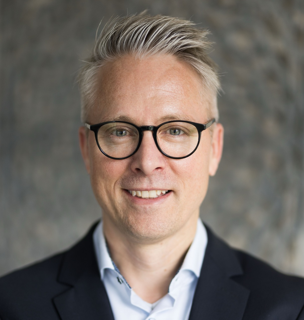 Das Bild zeigt den Autor. Ein professionelles Foto eines Mannes mit graumellierten Haaren und Brille. Er lächelt leicht in die Kamera.