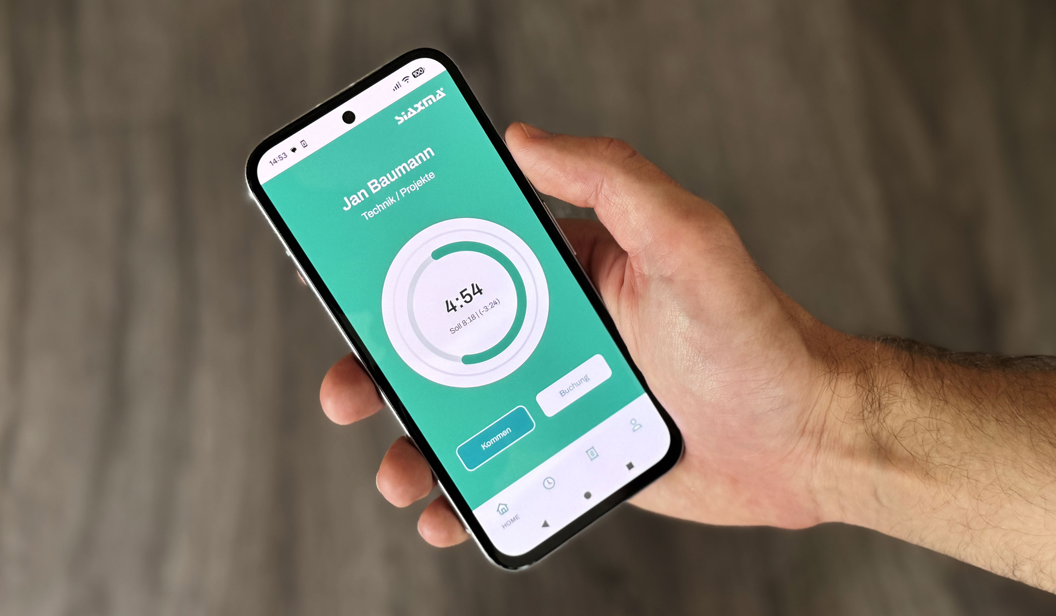 Nahaufnahme einer Hand, die ein Smartphone vor einem unscharfen, graubraunen Hintergrund hält. Auf dem Display ist eine App mit grünem Interface der Firma „SIAXMA“ zu sehen. Angezeigt wird das Profil von „Jan Baumann“ aus der Abteilung „Technik / Projekte“. Im Zentrum steht eine runde Zeitanzeige mit dem Wert „4:54“ und der Info „Soll 8:18 | (-3:24)“. Am unteren Bildschirmrand sind die Buttons „Kommen“ und „Buchung“ platziert.