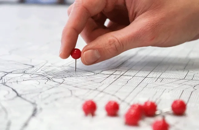 Closeup einer Hand, die Stecknadeln in eine Karte steckt; Symbolbild für die unterschiedlichen Punkte eines Roadmaps für KI.