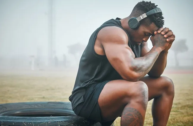 Spitzensportler stützt den Kopf mit seinen Händen um sich mental auf das bevorstehende Training vorzubereiten.
