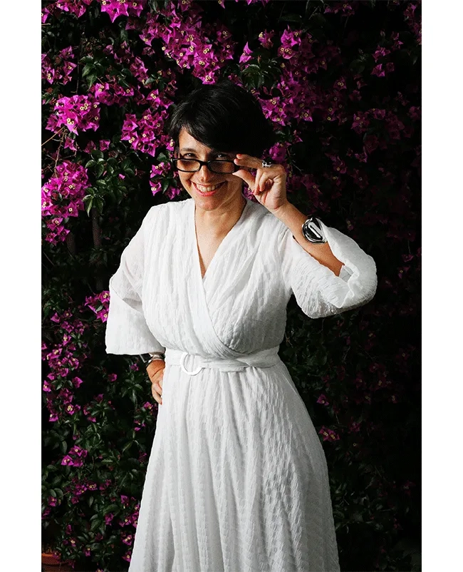 Vanessa Marcie steht vor einem blühenden Busch und blickt humorvoll über ihre Brille