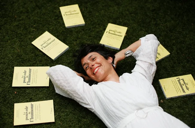 Vanessa Marcie liegt auf einer Wiese. Um sie herum steht ihr Buch le pouvoir de l'humour, die macht des humors