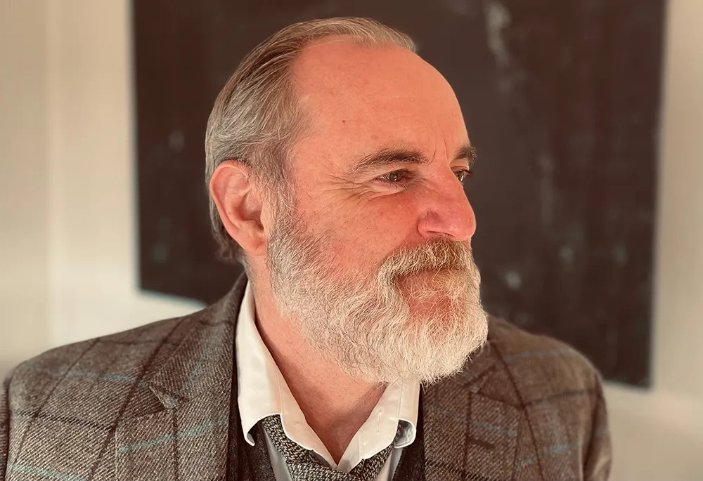 Das Bild zeigt Psychoanalytiker Peter Schneider im Halbprofil, er hat nach hinten gekämmte graue Haare, einen weissen Bart und lächelt. Er trägt ein Hemd und ein gemustertes Tweed-Jackett.