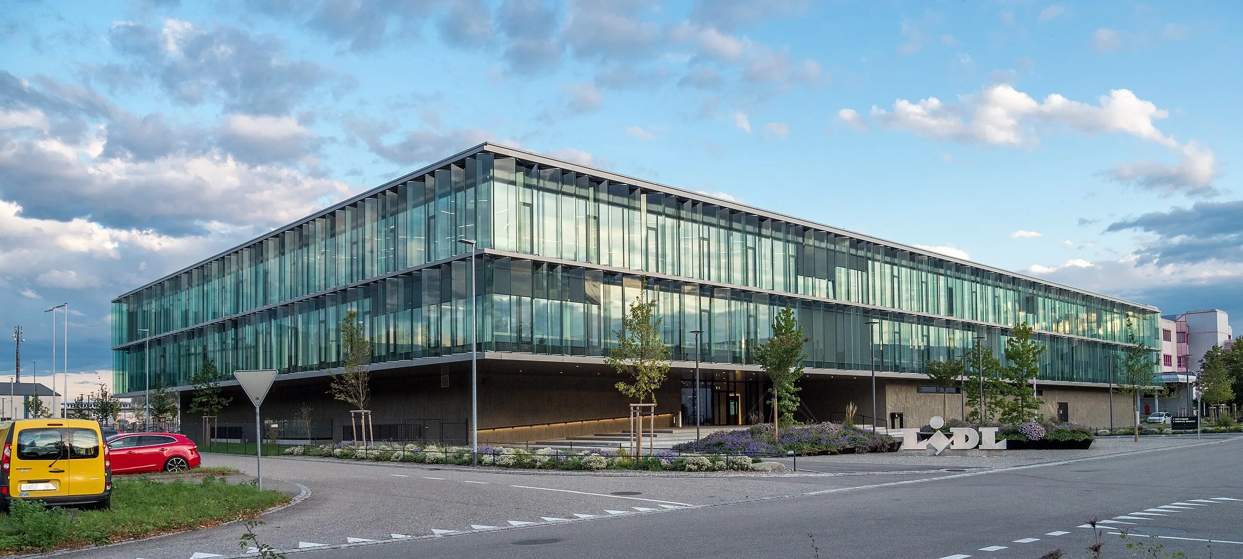 Das Bild zeigt den Firmensitz von Lidl Schweiz in Weinfelden, ein grosser, flacher, verglaster Bau in modernem Stil.