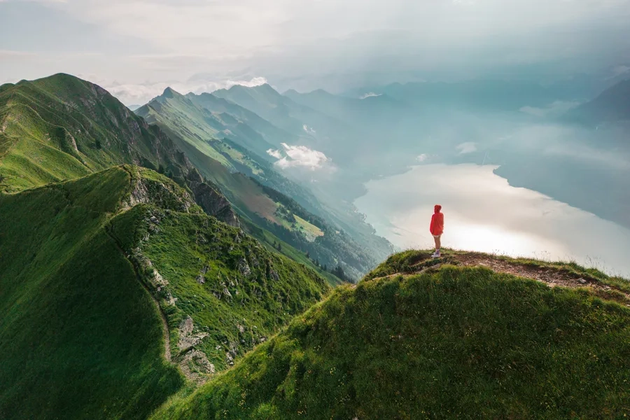 Vue aérienne d'une femme vêtue d'un manteau rouge debout au sommet de la crête montagneuse Augstmatthorn.