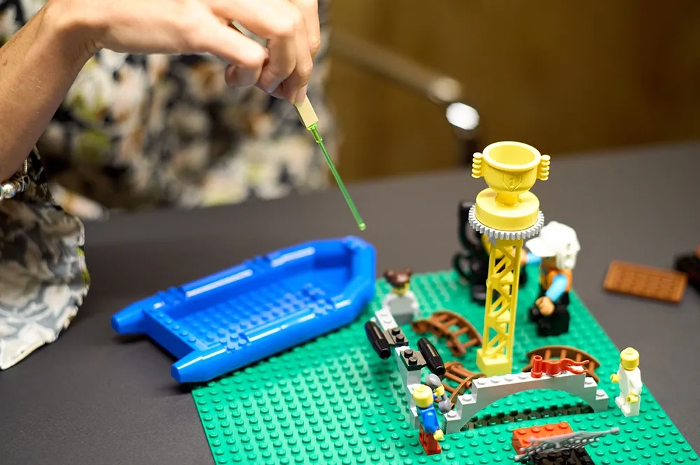 Ein Lego-Set mit grüner Unterlage, ein Schlauchboot und ein Turm (?) - das Bild zeigt eine Lego Serious Play Session
