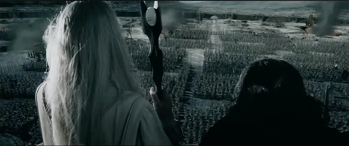 Eine Gegenüberstellung zweier Bilder mit starken visuellen Parallelen in der Darstellung von Massenaufmärschen: Das erste Bild zeigt eine Szene aus den "Herr der Ringe"-Filmen. Man sieht Saruman in weißen Roben mit seinem Stab und Gríma Schlangenzunge von hinten auf einem Balkon stehen. Sie blicken von oben auf das Industriegelände von Isengard hinab, wo eine gigantische Armee von Uruk-hai in streng geometrischen, riesigen rechteckigen Blöcken angetreten ist. Im Hintergrund steigen dunkle Rauchschwaden auf.